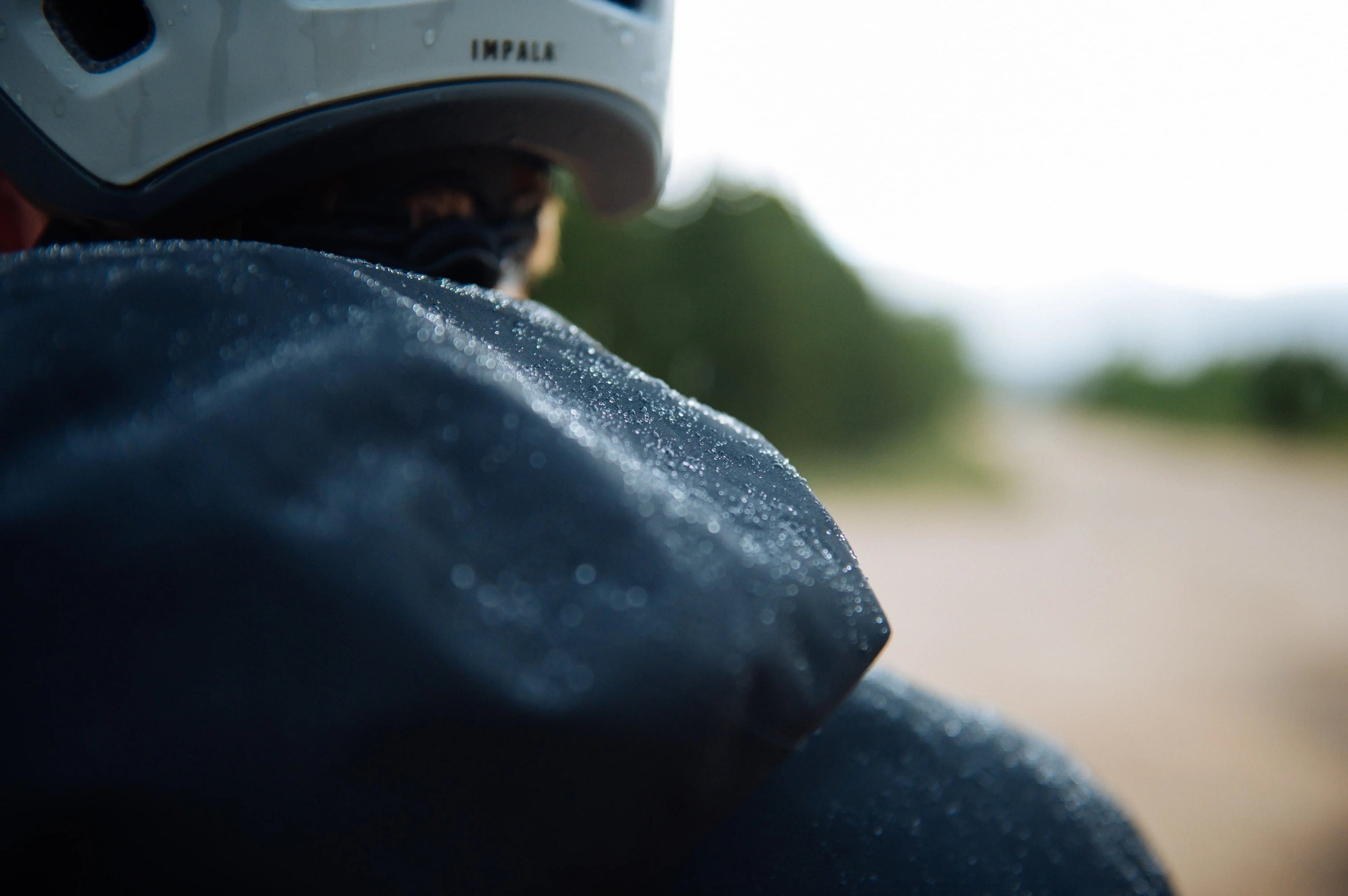 close-up image of the back of a mountain biker in helmet and black rain jacket with rain droplets